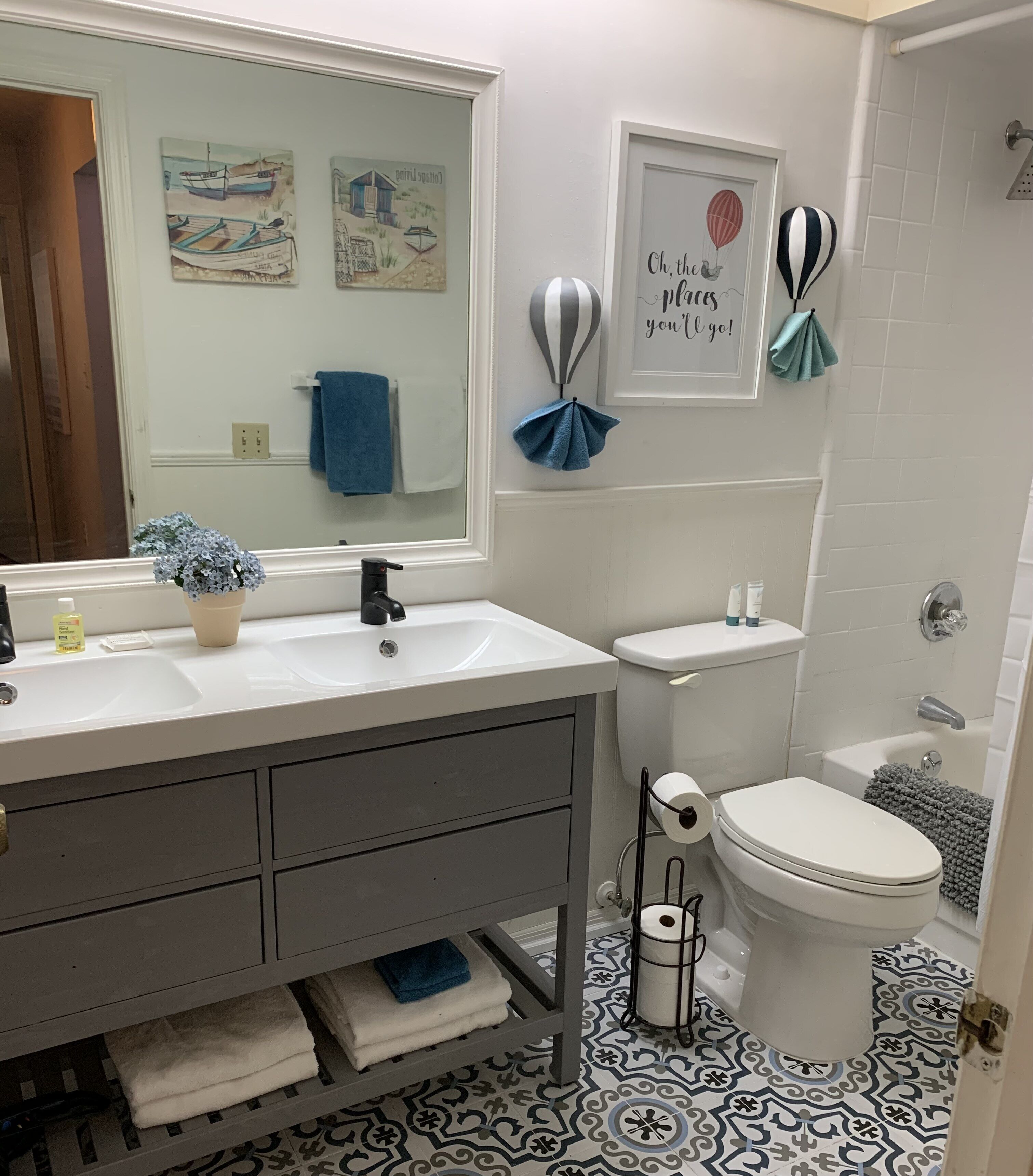 A bathroom with a double sink, toilet, and a shower area. There are towels and toiletries on the sink counter.