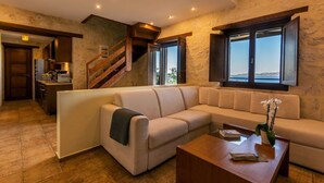 Ein modernes Wohnzimmer mit einem beigefarbenen Ecksofa, einem Holztisch und Meerblick durch große Fenster.