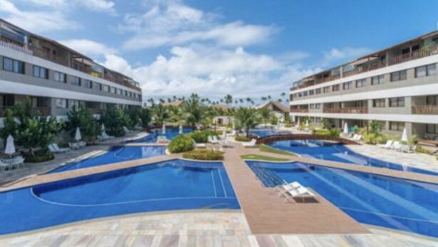A hotel with a large swimming pool, multiple balconies, and a clear sky.
