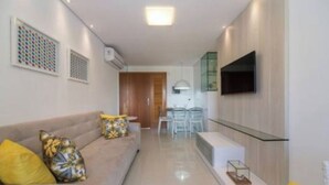 A modern living room with a sofa, a flat-screen TV mounted on the wall, and a dining area with chairs and a table.