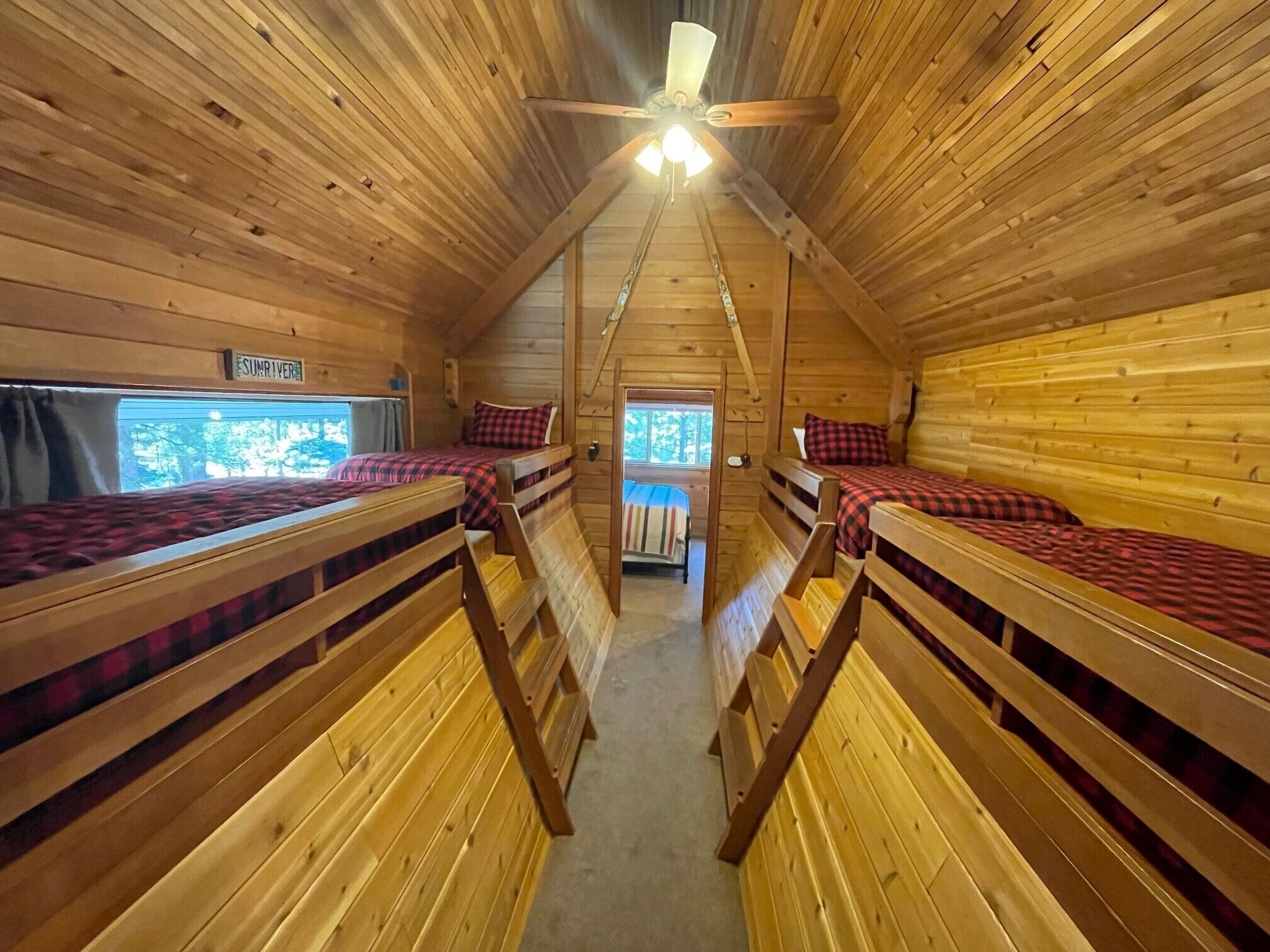 Une cabine équipée de quatre lits superposés disposés en forme de U, d’un ventilateur de plafond et d’une fenêtre donnant sur la forêt.
