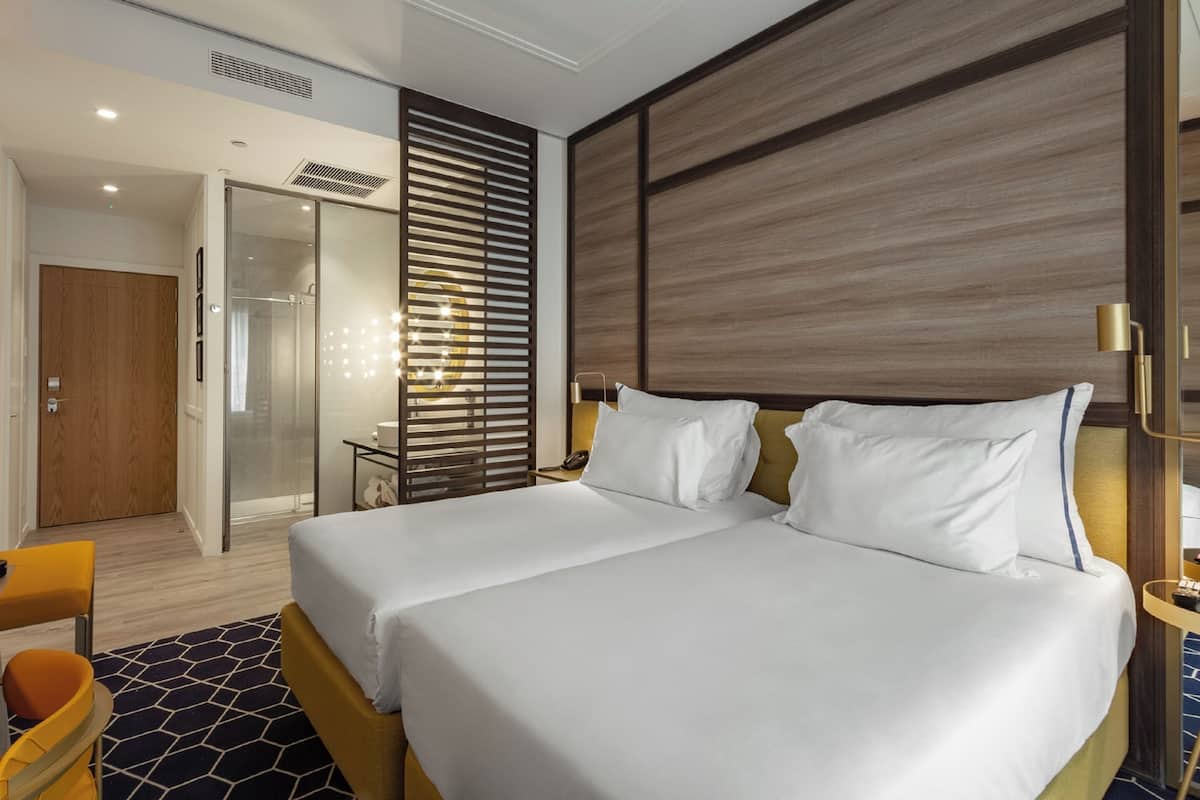 A hotel room with a large bed, a wooden headboard, a nightstand, a desk, and a chair.