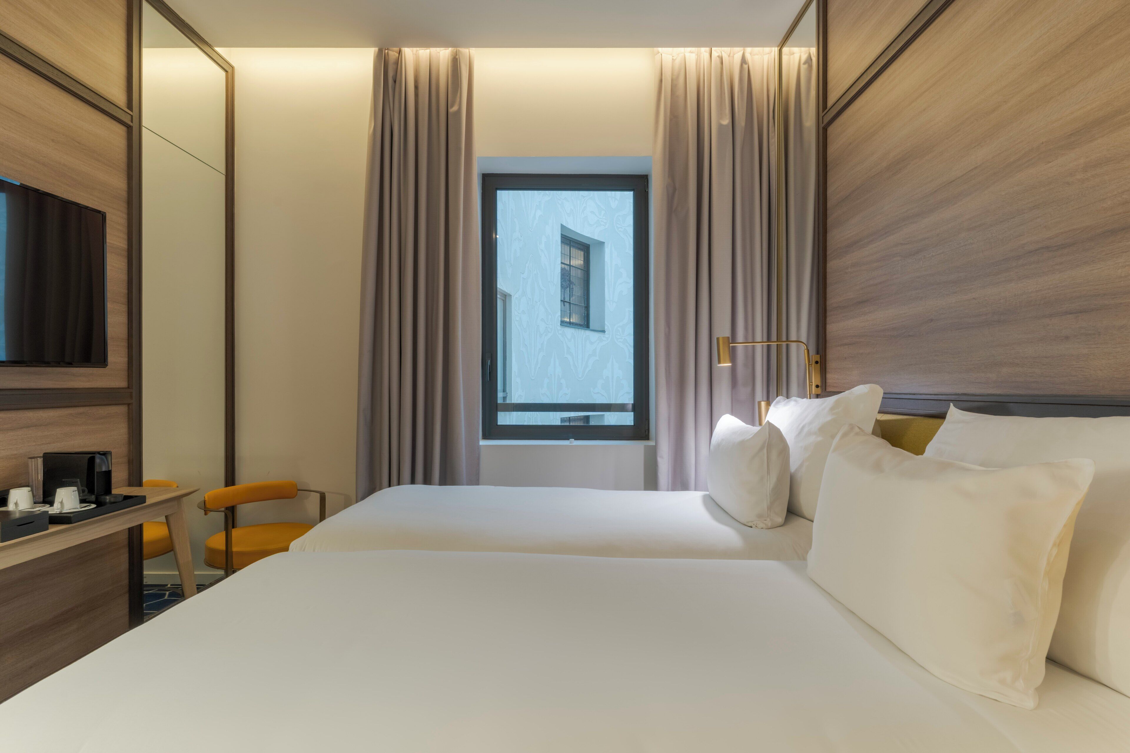 A hotel room with a bed, a desk, a chair, a television, and a window with curtains.