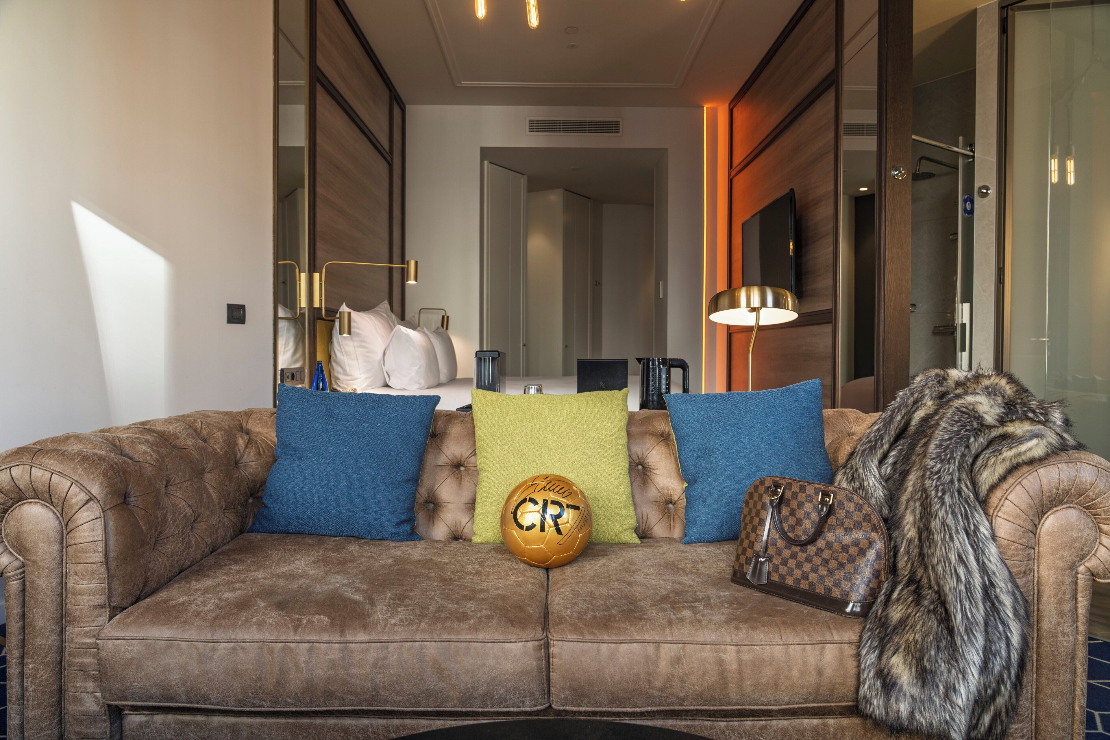 A brown leather sofa with blue and green cushions, a fur throw, and a sports ball.