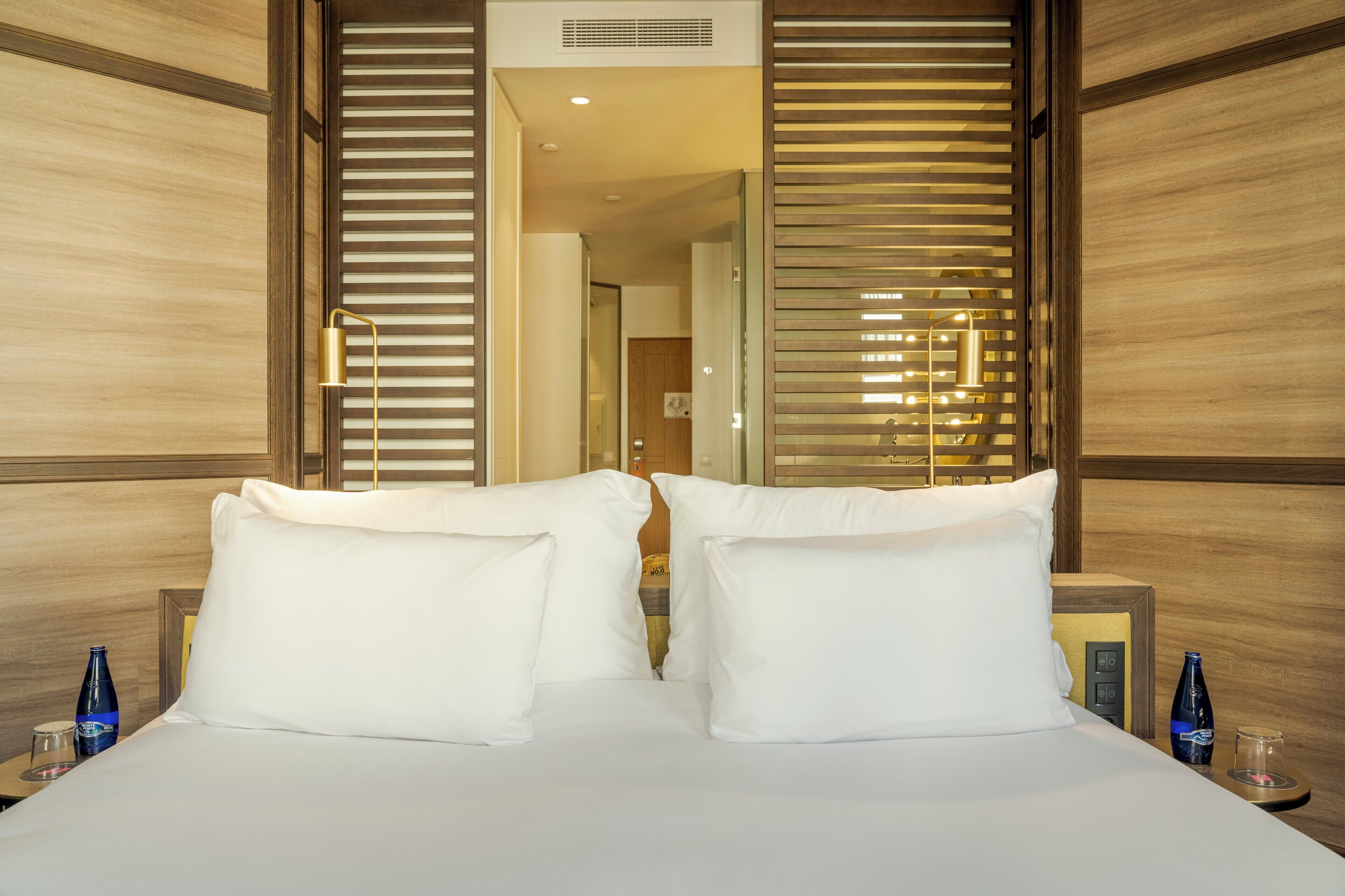 Habitación de hotel con una cama grande, dos mesitas de noche y un espejo que refleja la habitación.