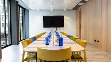 Une salle de conférence avec une longue table, des chaises jaunes et un grand écran.