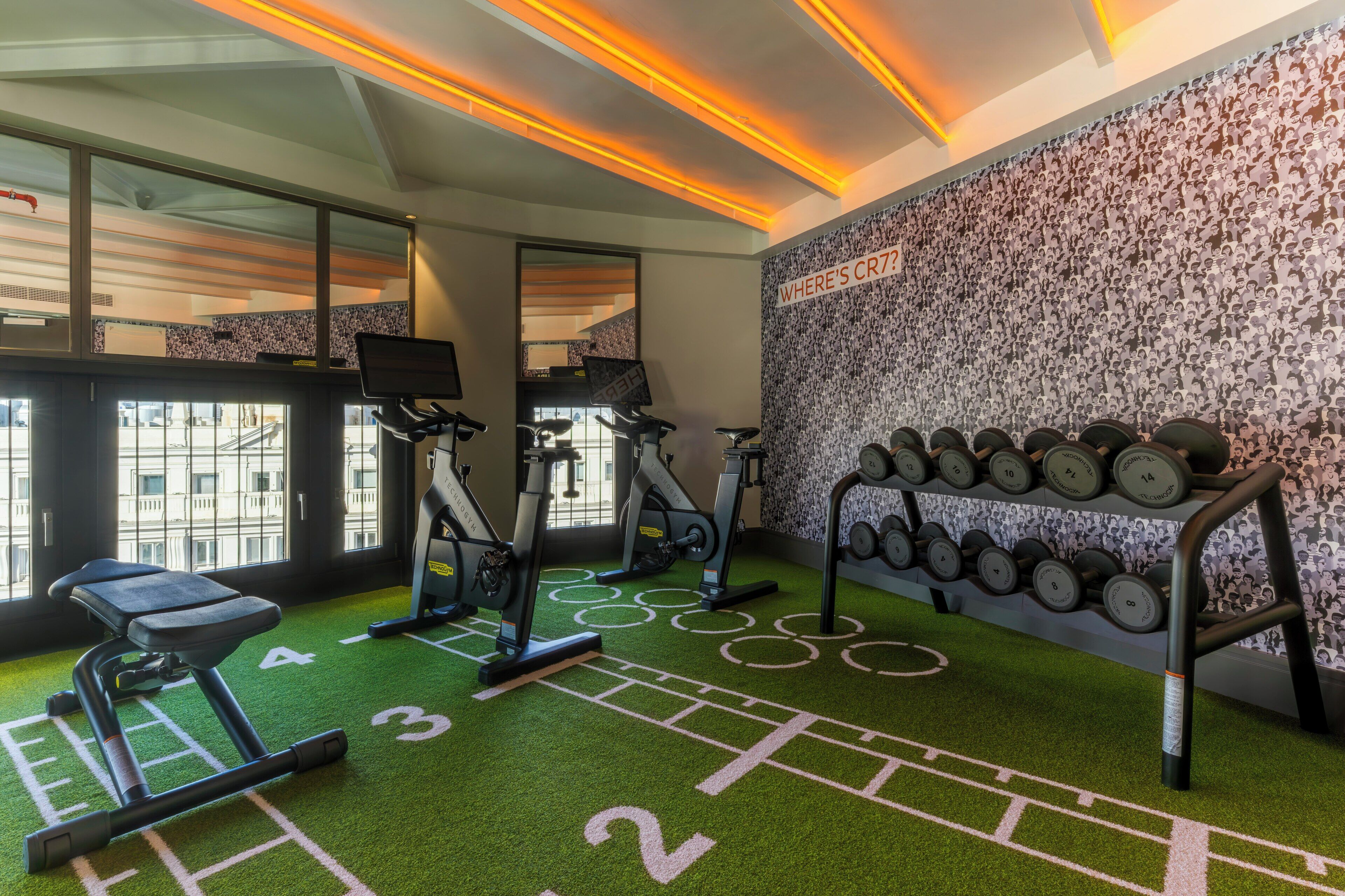 Una palestra con tapis roulant, cyclette ellittiche e una parete piena di manubri.