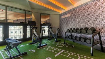 Una palestra con tapis roulant, cyclette ellittiche e una parete piena di manubri.