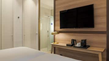 Ein Hotelzimmer mit einem Bett, einem an der Wand befestigten Fernseher, einem Nachttisch mit Lampe und einer Dusche.