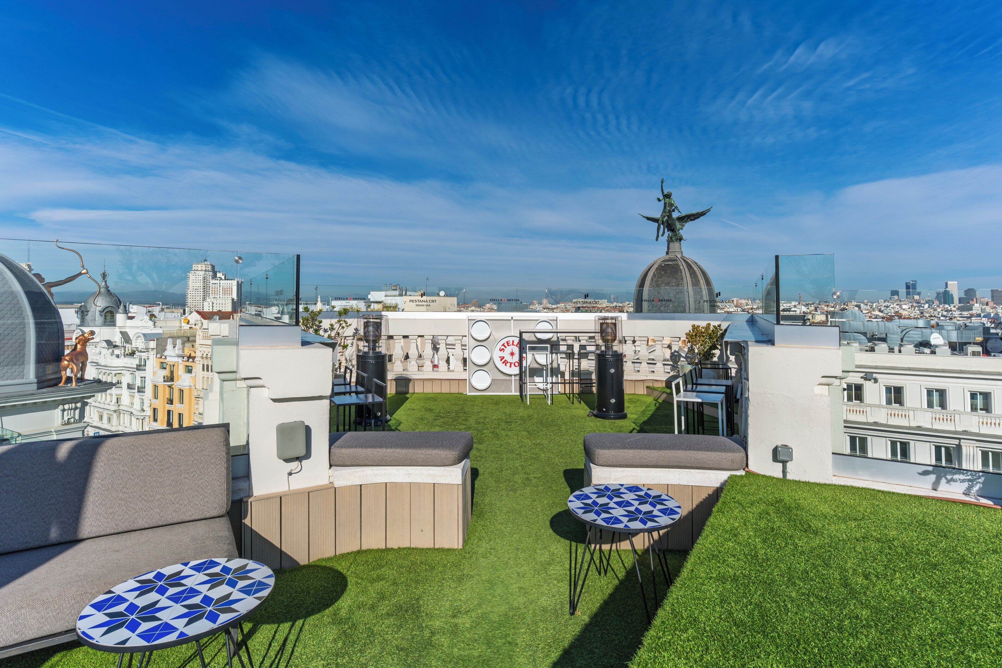 A rooftop terrace with seating, a statue, and a city view.