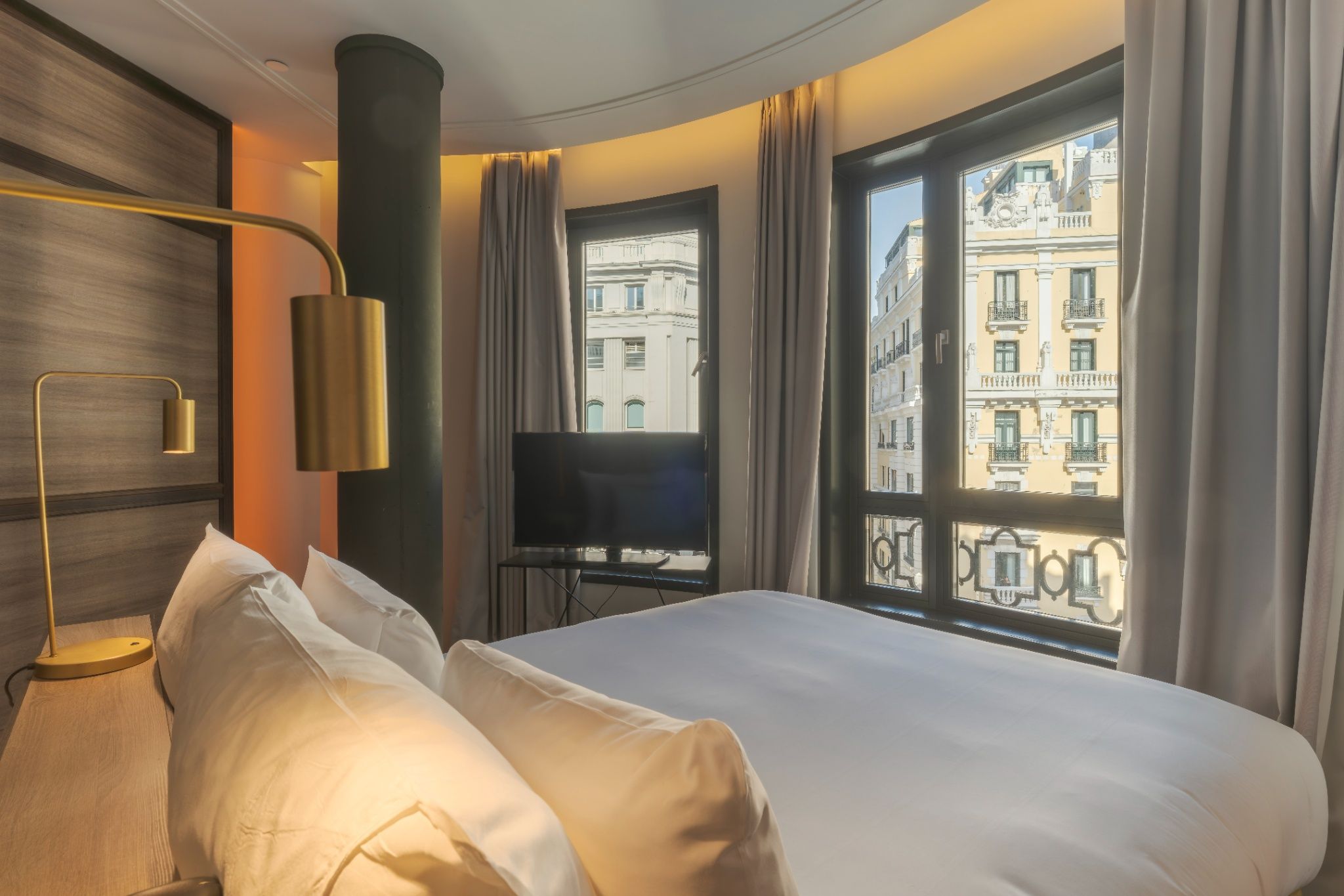 Ein Hotelzimmer mit einem großen Bett, einem Flachbildfernseher und Blick auf ein Gebäude.
