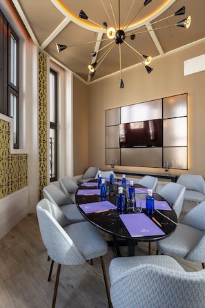 A conference room with a round table, multiple chairs, a large flat-screen TV, and a modern ceiling light fixture. - Pestana CR7 Gran Vía Madrid (Madrid)