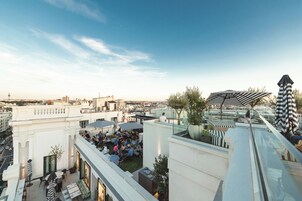 Eine Dachterrasse mit Außenbestuhlung, einer Glasbrüstung und Blick auf die Stadtlandschaft.