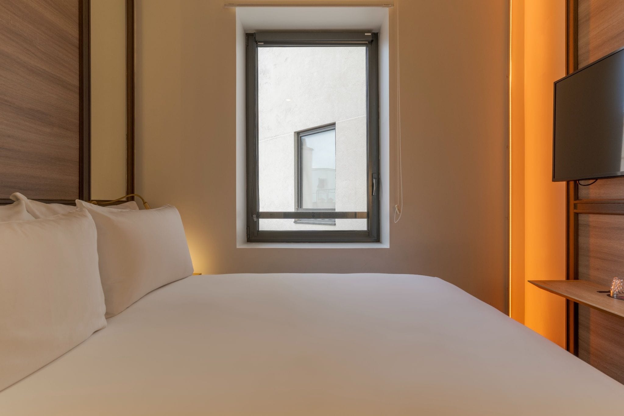 A hotel room with a large bed, a window, and a television on the wall.