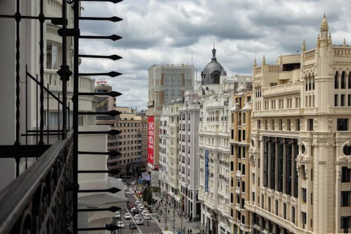 Una calle de la ciudad con edificios históricos, incluyendo un edificio blanco destacado con una cúpula y un estandarte rojo.
