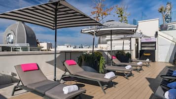 Un área de lounge en la azotea con sillones de sol, sombrillas a rayas y vistas de la ciudad.