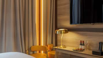 A hotel room with a bed, a desk with a lamp, a TV mounted on the wall, and a chair.