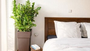 Ein Schlafzimmer mit hölzernem Kopfteil, weißer Bettwäsche, einem Blumentopf, einem Nachttisch mit einem Buch und einem gerahmten Bild an der Wand.