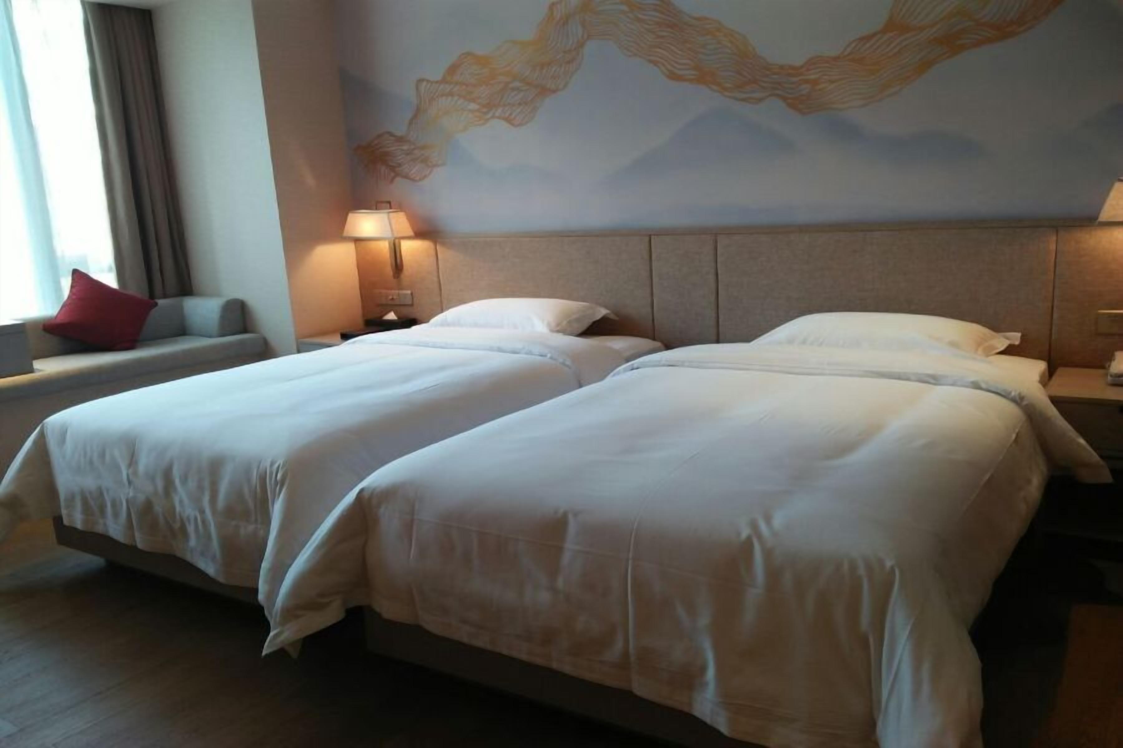 Habitación de hotel con dos camas, una mesita de noche, una lámpara y un mural abstracto grande en la pared.