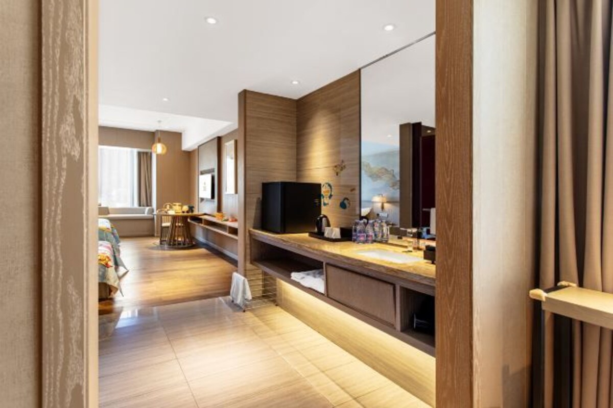 A modern hotel room with a wooden floor, a large mirror, a flat-screen TV, and a small kitchenette.