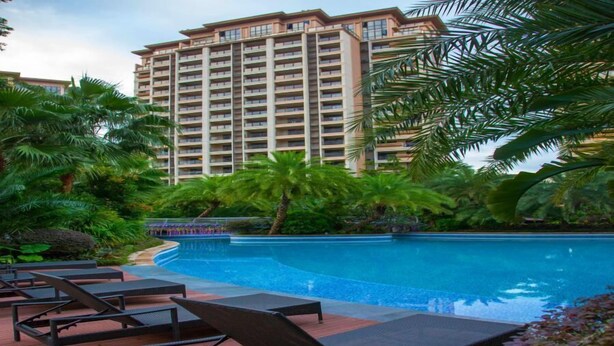 A poolside area with lounge chairs, a swimming pool, and a high-rise building in the background.