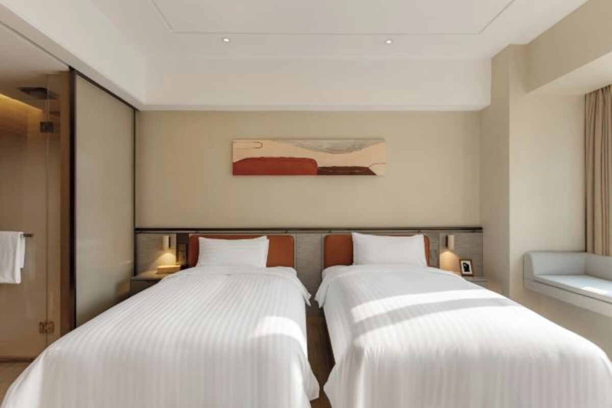A hotel room with two beds, a painting on the wall, and a bedside table with a lamp.