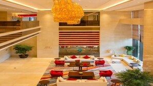 A modern lobby with a central seating area, a staircase, and a large chandelier.