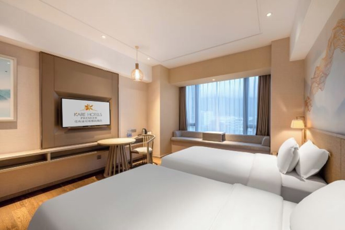 A hotel room with two beds, a TV, a desk with a chair, and a window with a view.