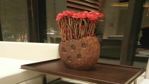 A wooden vase with a unique design on a dark wooden tray.