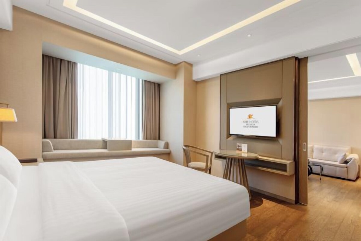 Une chambre d’hôtel moderne dotée d’un grand lit, d’un coin salon avec un canapé et des fauteuils, d’un téléviseur fixé au mur et d’une petite table avec une lampe.