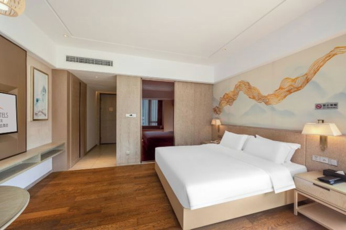 A hotel room with a large bed, bedside tables, a TV, and a mural on the wall.