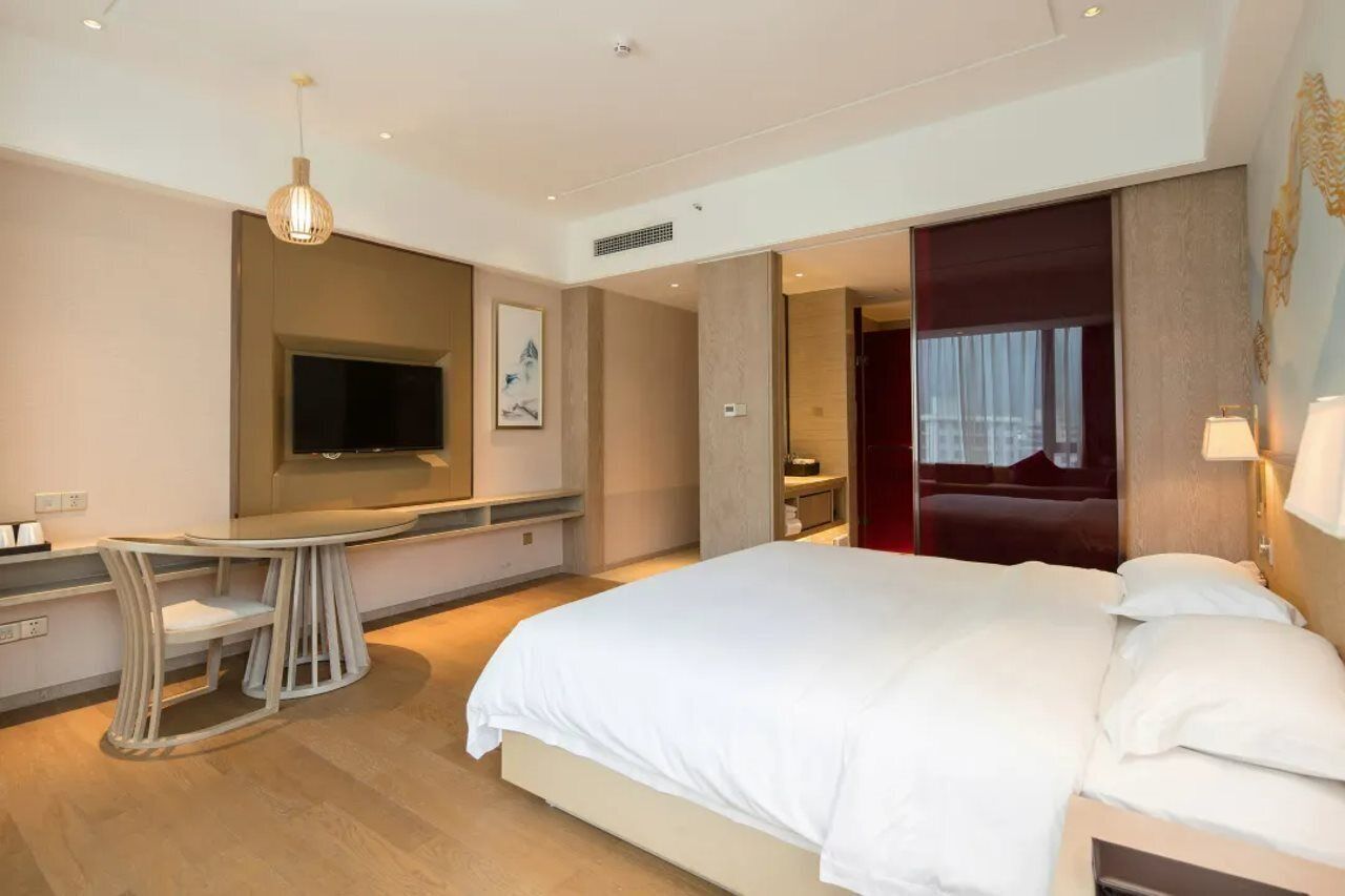 Habitación de hotel moderna con una cama grande, un escritorio con silla, un televisor de pantalla plana y una pared de acento roja.