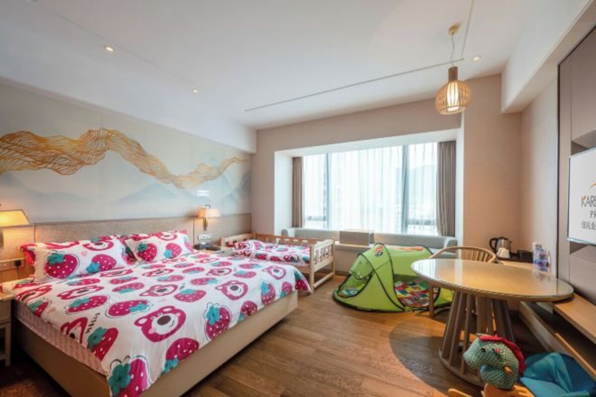 A hotel room with a bed, a green play tent, a round table, and a large window.