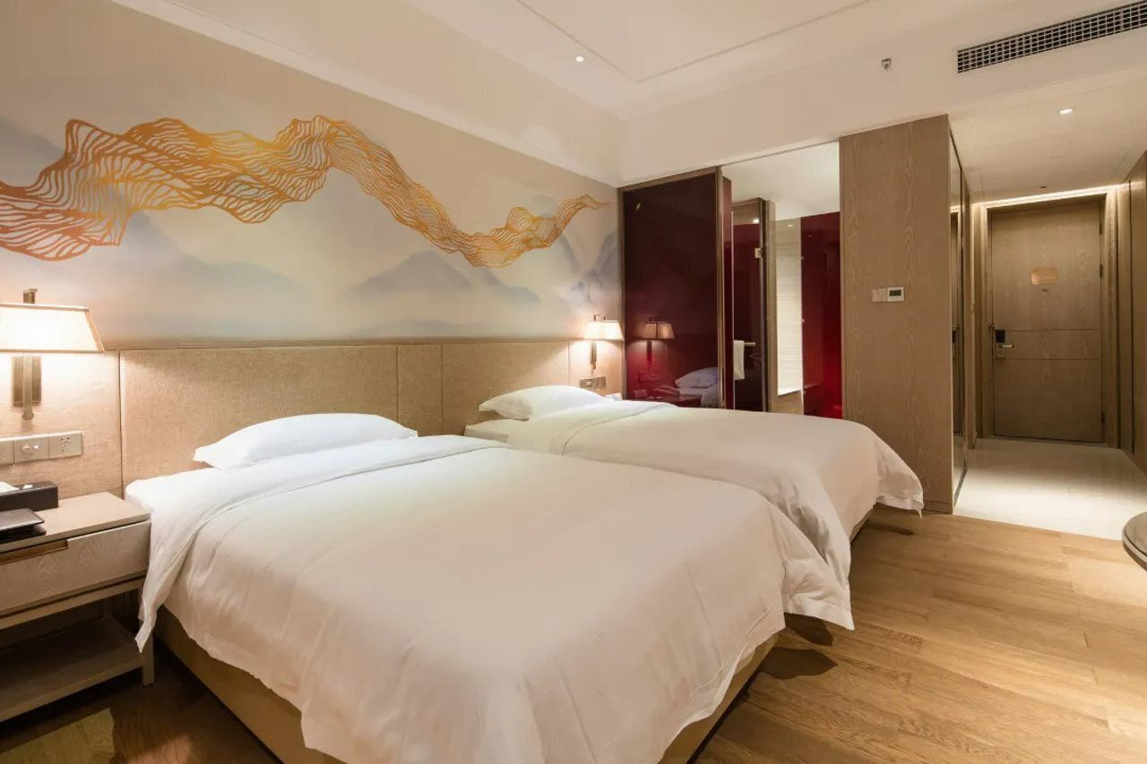 Habitació d'hotel amb dos llits, un mural a la paret, una tauleta de nit i una porta que dona a un bany.