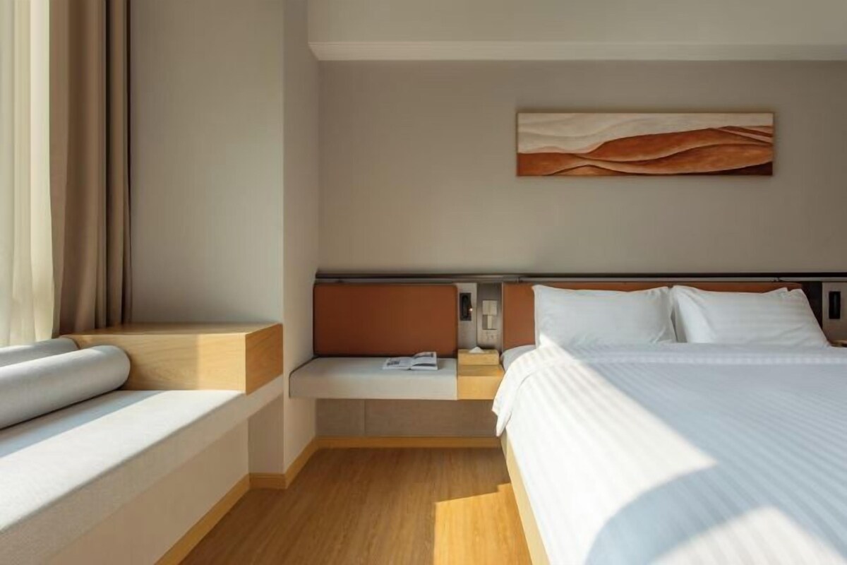 A modern hotel room with a large bed, a bedside table, a reading light, and a wall-mounted artwork.