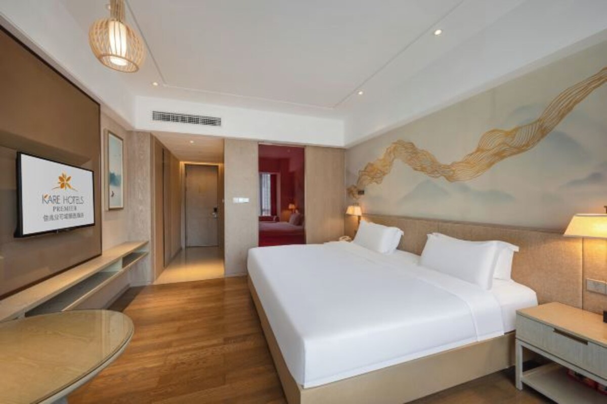A hotel room with a large bed, a bedside table, a TV mounted on the wall, and a painting on the wall.