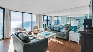 A spacious living room with a large window offering a view of the ocean, a leather sofa, a glass coffee table, and a television.
