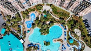 An aerial view of a resort with multiple swimming pools, palm trees, and lounge areas.