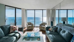 A spacious living room with a large view of the ocean, two sofas, a coffee table, and two armchairs.