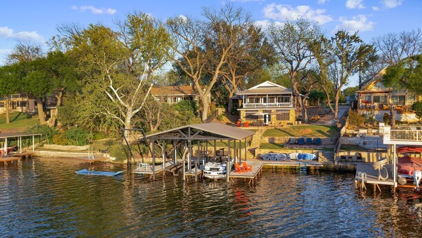 A lakeside property with a dock, a covered seating area, and a large house with a balcony. - Private Boat Slip| Lakefront | Putting Green | Firepit (Burnet)
