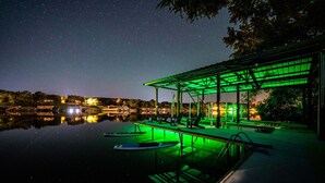 A nighttime view of a waterfront area with a covered seating area, a pool, and a dock with boats. - Private Boat Slip| Lakefront | Putting Green | Firepit (Burnet)