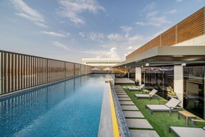 A rooftop pool with a clear view of the sky, a wooden deck, and lounge chairs.