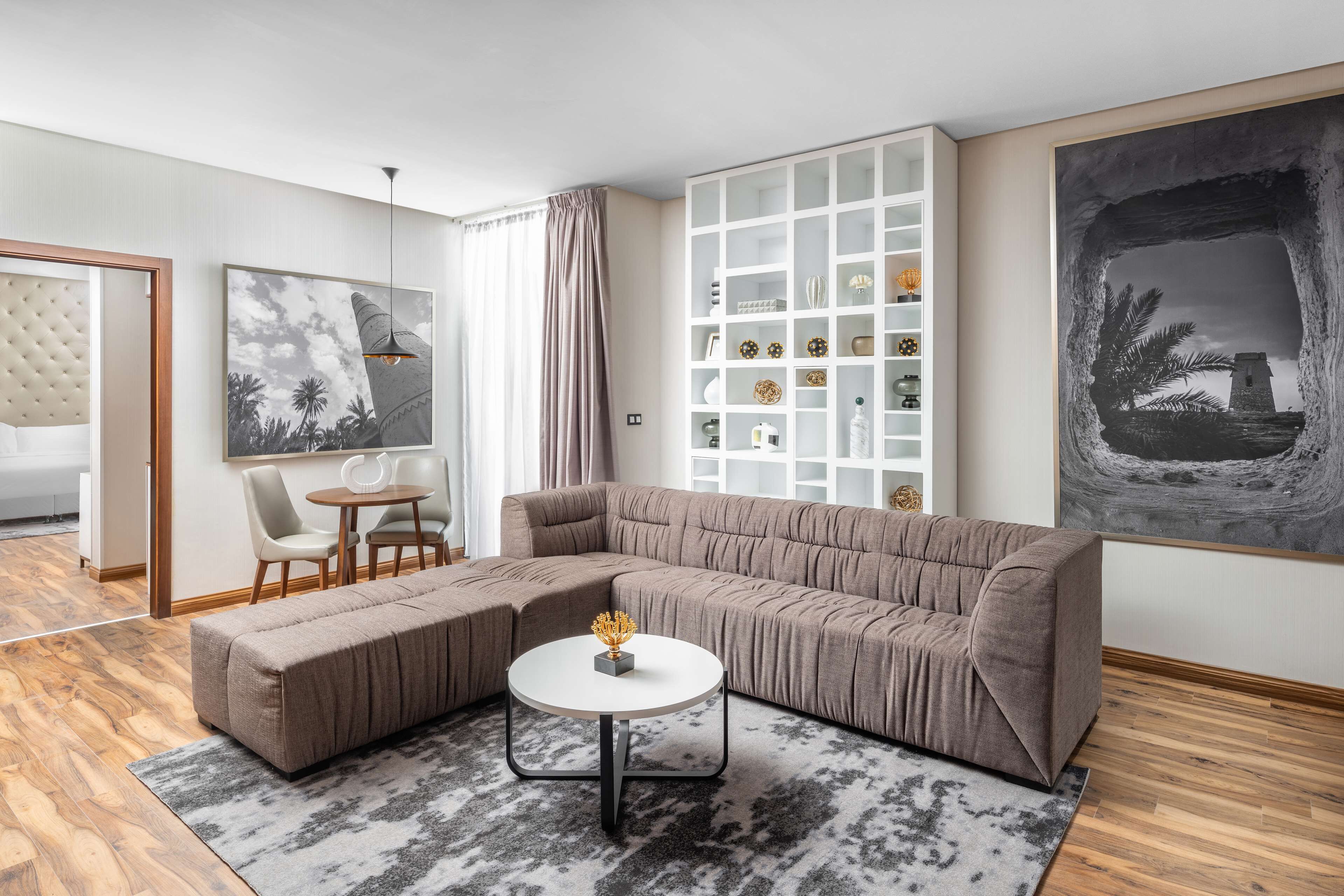 A modern living room with a sectional sofa, a round coffee table, and a white shelving unit against the wall.