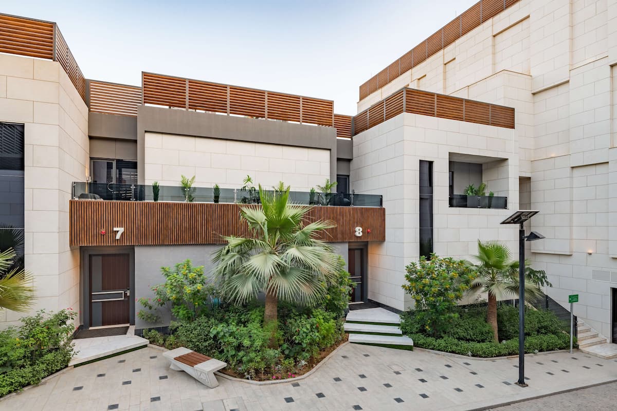 A modern building with a courtyard featuring a palm tree, a bench, and a solar-powered street lamp.
