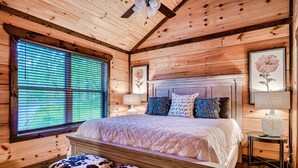 Une chambre dans une cabane en bois, avec un grand lit, un banc et une fenêtre équipée de stores.