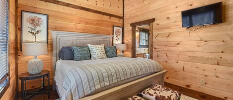A wooden cabin bedroom with a bed, two nightstands, a ceiling fan, and a mounted TV.