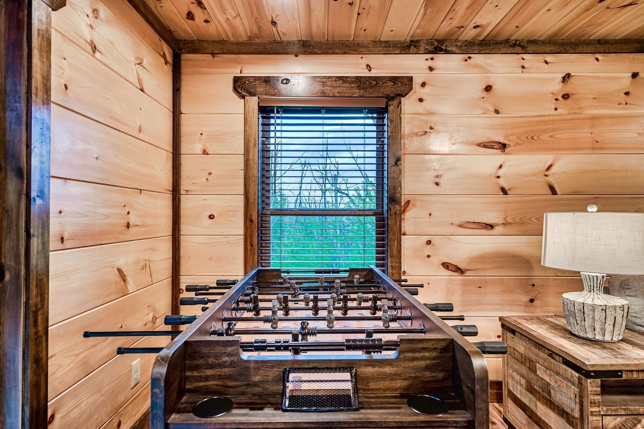 Una habitación de madera con mesa de fútbol y ventana con persianas.