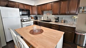 Una cocina con armarios de madera, un refrigerador de acero inoxidable, una encimera de granito y una mesa de comedor de madera.