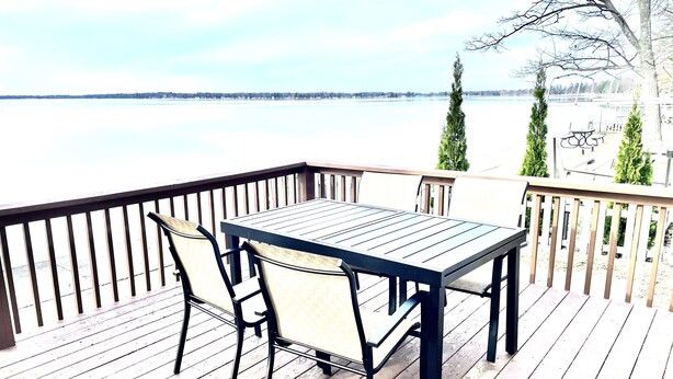 Una terraza de madera con mesa y sillas con vista a un cuerpo de agua.