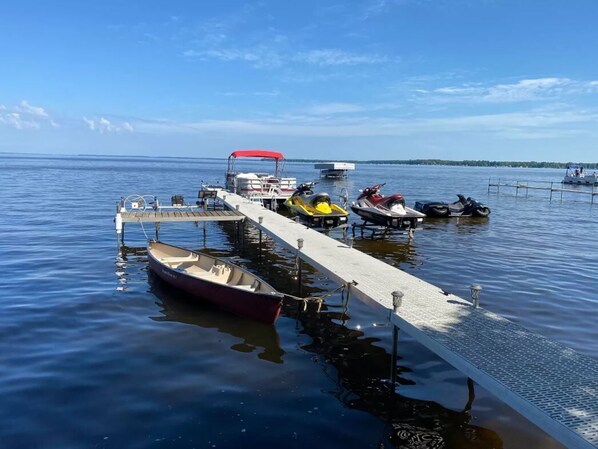 Un quai où sont amarrés divers types d’embarcations, notamment un bateau rouge, un jet ski jaune et un bateau blanc doté d’un auvent rouge.